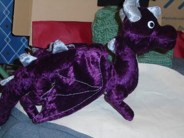 The dragon is made in rich purple velour with silver grey contrasts, and has wobble eyes.