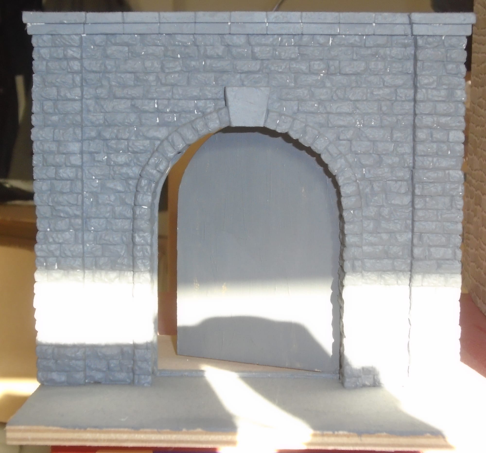 Arched wooden doorway set in a brick wall, all painted grey.