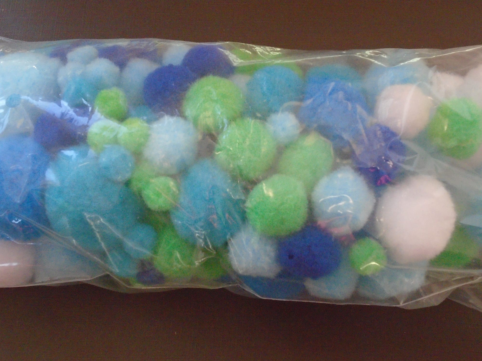 A bag of pompoms in assorted sizes and shades of blue, green, and white.