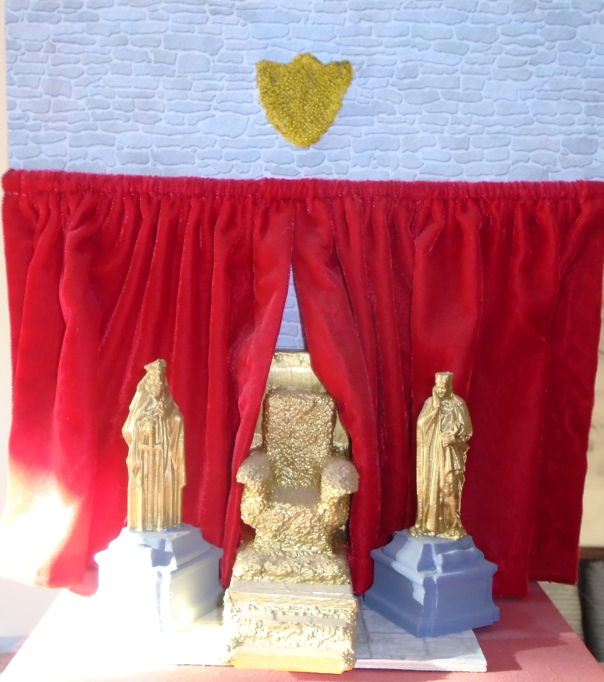 Throne room set, with a gold throne, gold statues on grey plinths, and red velvet curtains over stonework.