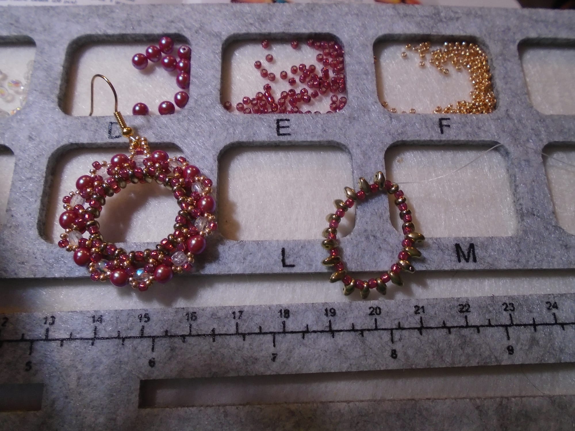 One finished wreath earring and one just started, on a bead tray containing different types of beads.