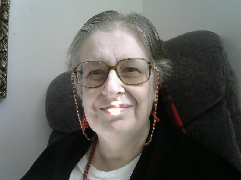 I have short straight grey hair, large glasses with a handmade beaded chain, red star earrings, and a smile.