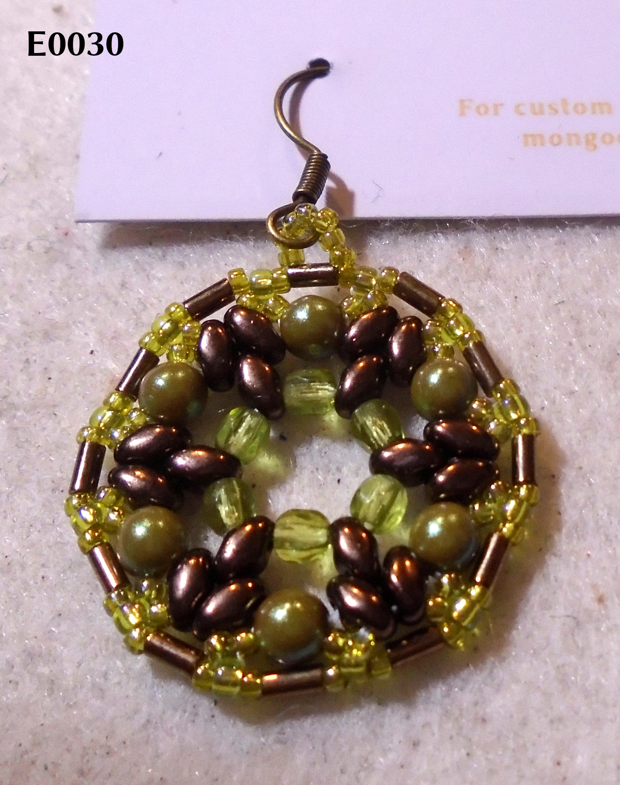 1920s-style round earring in dark bronze set against shades of olive/peridot green.