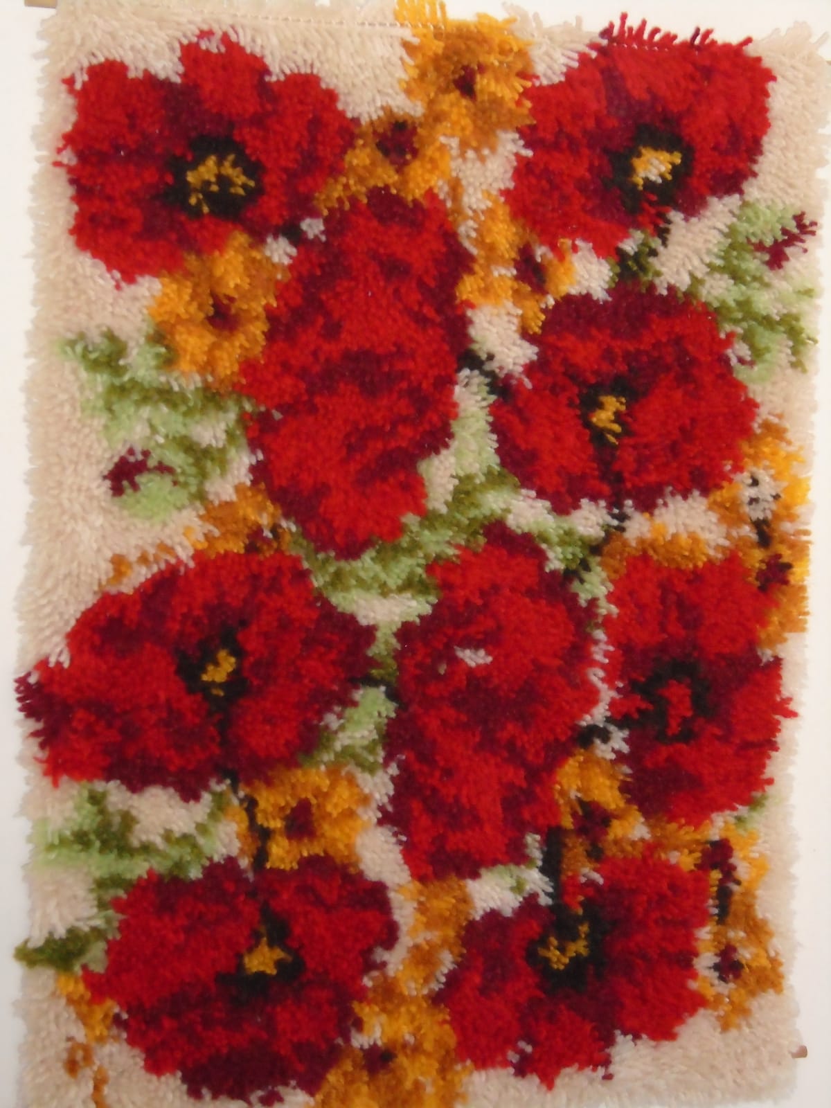 Large latch hook rug wall hanging, featuring red poppies and small yellow flowers on an ecru background.