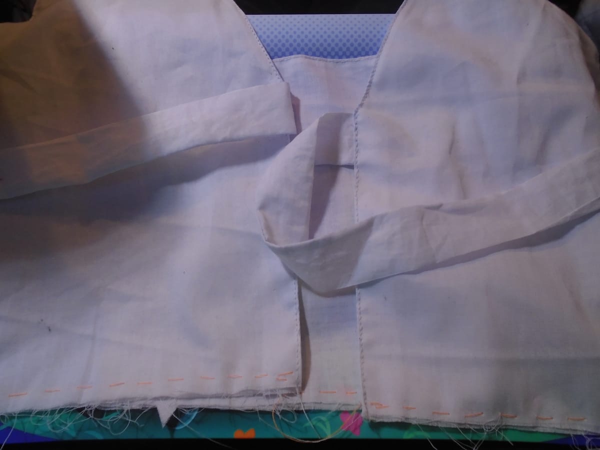An empire-waist pinafore bodice with a pair of ties at the base of the V back neck.  It is made in fine white lawn.