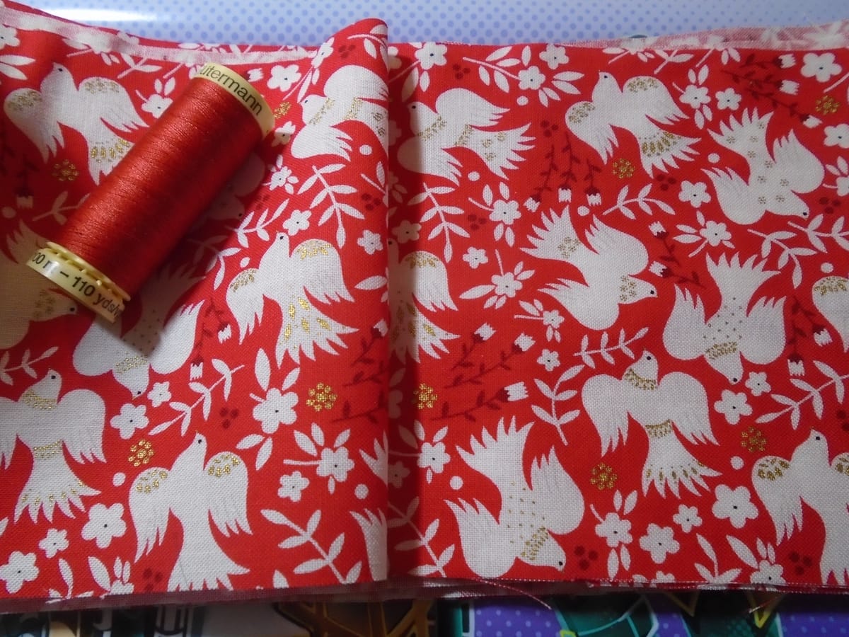 A strip of fabric 12 cm wide, with matching thread. It has white birds in flight on red, with burgundy and gold details.