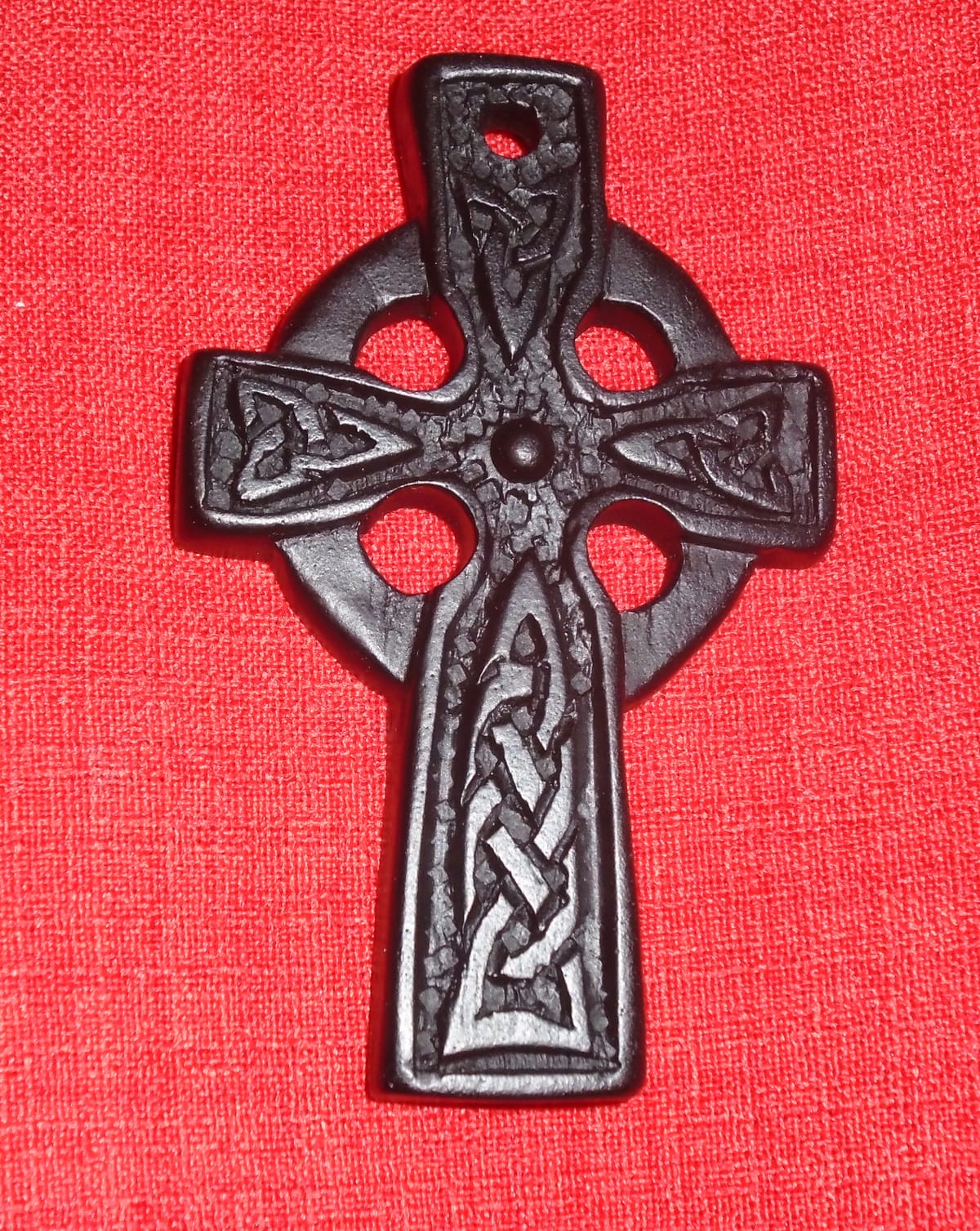 Very dark brown Celtic cross with knotwork and background circle, shown against a red linen-look fabric.