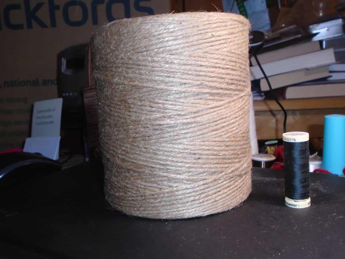A very large cylindrical spool of natural-coloured jute twine sitting next to a reel of regular sewing thread
