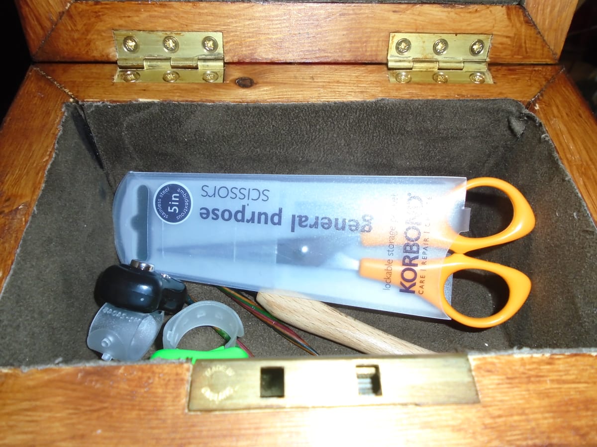 Wooden box containing small scissors, row counters, cable needles, and a crochet hook for picking up stitches.
