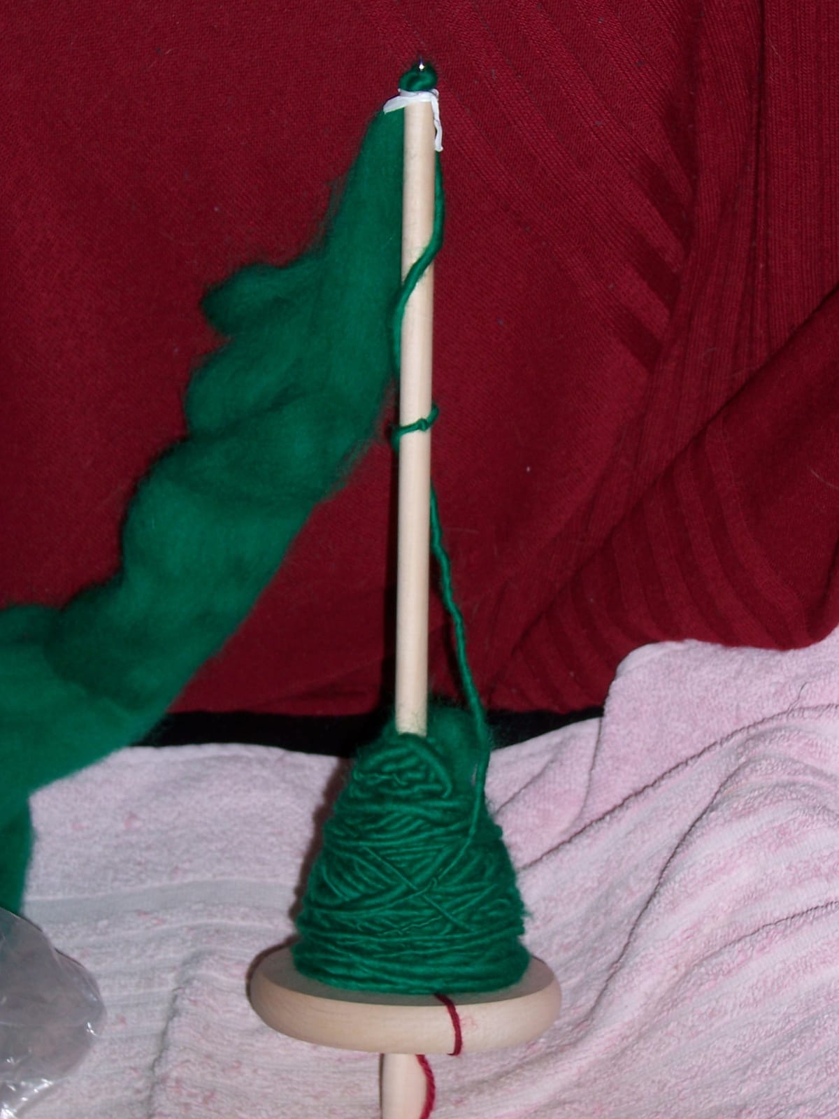 About 50 g of green yarn wound onto a drop spindle. There is also a piece of red yarn at the bottom (the "leader").