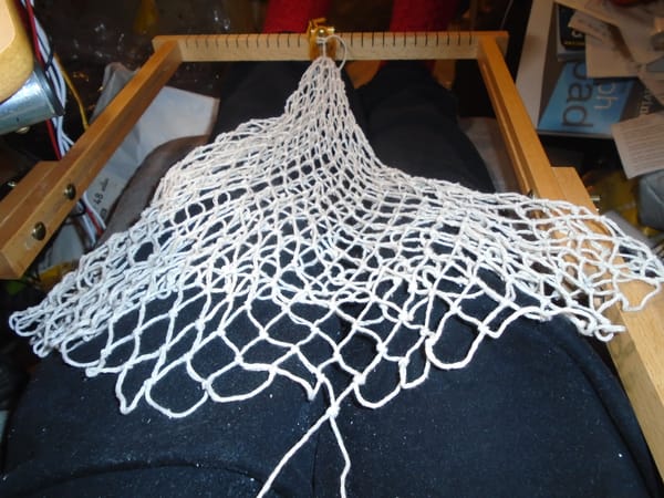 String bag, almost ready to add the handles, on a netting frame.  It is made from white cotton string.