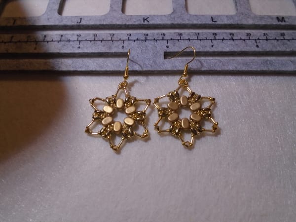A pair of large but delicate six-pointed star earrings made from gold-coloured beads.  The central ones are semi-matte.
