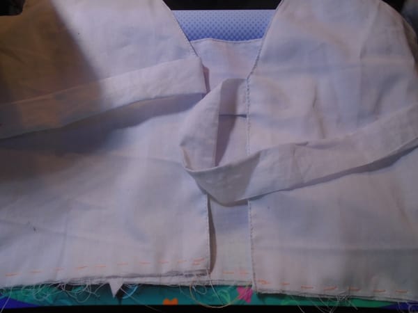 An empire-waist pinafore bodice with a pair of ties at the base of the V back neck.  It is made in fine white lawn.