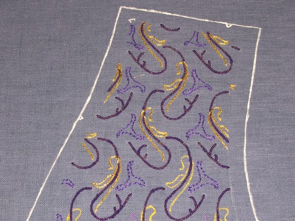 Purple and gold embroidery on air-force blue fabric.  The design is regularly repeating and somewhat botanical.