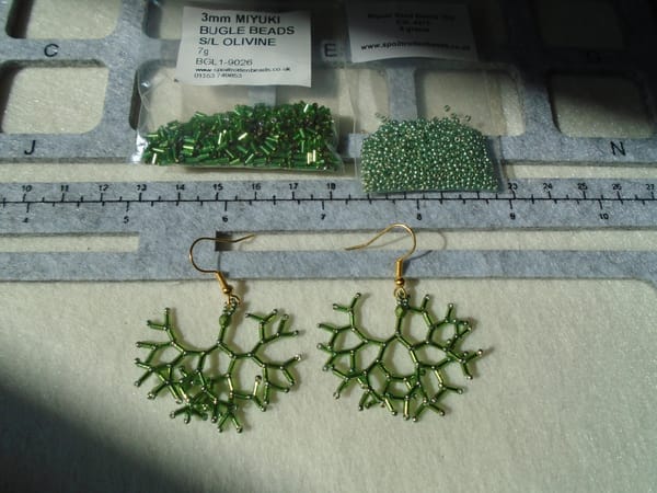 A second pair of bifurcating earrings, this time in olive green.  The beads used are also shown above them in bags.