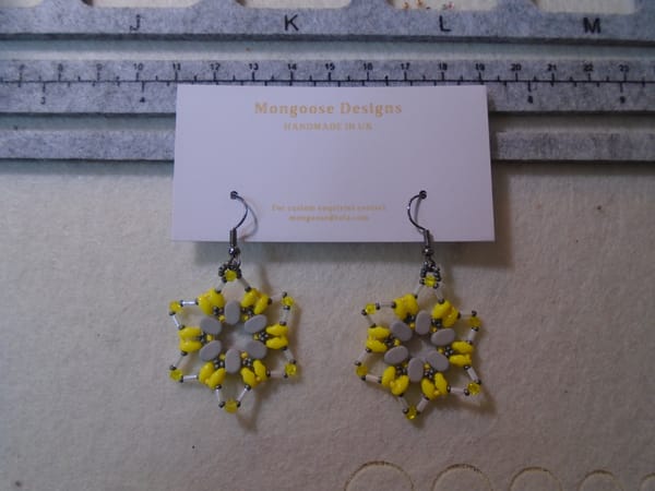 Yellow star earrings, on a card, with greyscale contrasts and gunmetal earwires.