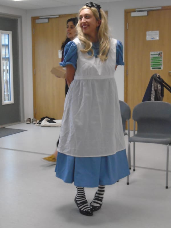 Alice in classic costume: blue dress with puffed sleeves; white pinafore; striped stockings; black shoes and headband.