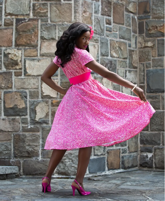 This is a rear view of a model wearing the dress in a small pink floral print, with wide fuchsia belt.