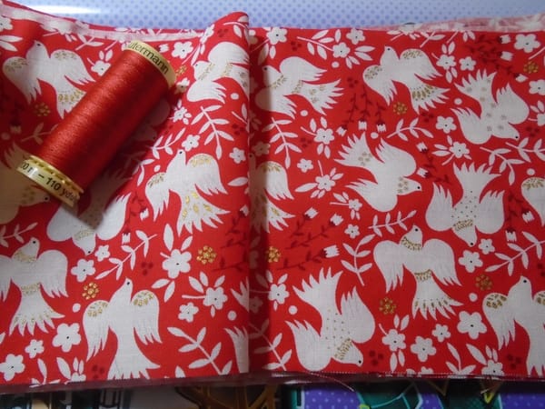 A strip of fabric 12 cm wide, with matching thread.  It has white birds in flight on red, with burgundy and gold details.