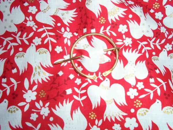 A simple copper penannular brooch pinned to a piece of closely-woven cotton fabric (it's the birds print from earlier).