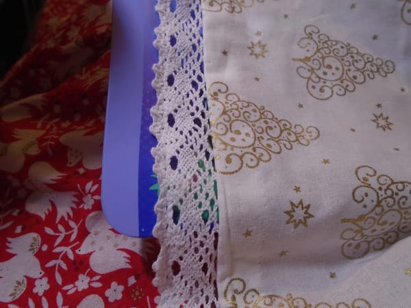 Off-white cotton fabric with a gold print, edged with white cotton lace which looks like bobbin lace (but probably isn't).