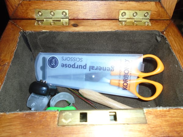 Wooden box containing small scissors, row counters, cable needles, and a crochet hook for picking up stitches.